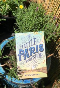 front cover of the little paris bookshop by nina george surrounded by lavender in a sun filled garden bed